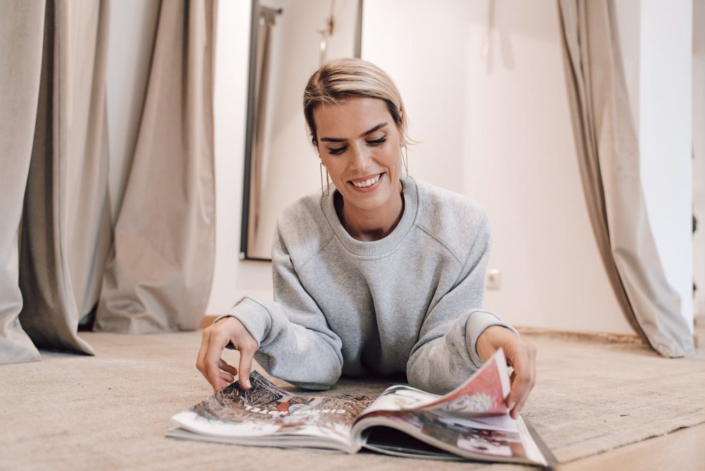 smiling woman turning pages of magazine lying on floor